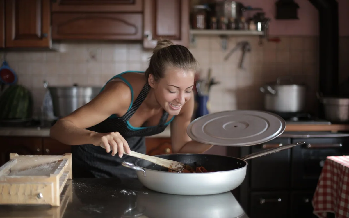 A person removing a crisp tray of food from an air fryer in a home kitchen