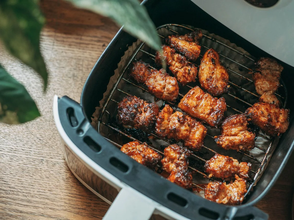 A basket air fryer on a kitchen counter with vegetables ready for cooking