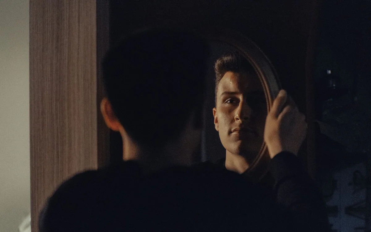 A person checking grooming details in a well-lit bathroom mirror