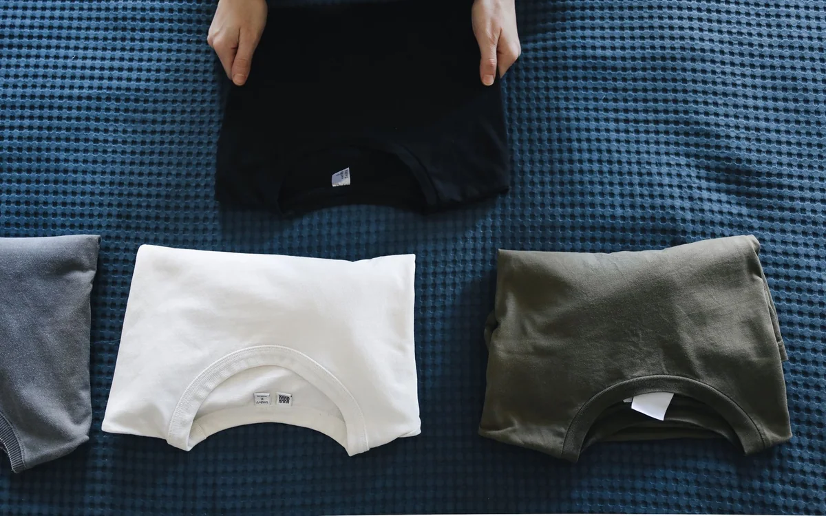 Clean laundry being folded beside a compact washing machine in an apartment