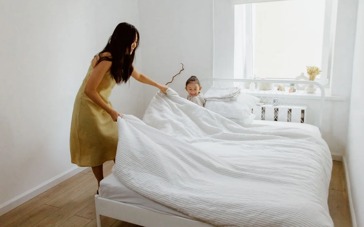 A parent making a bed with a waterproof mattress cover and cotton sheets